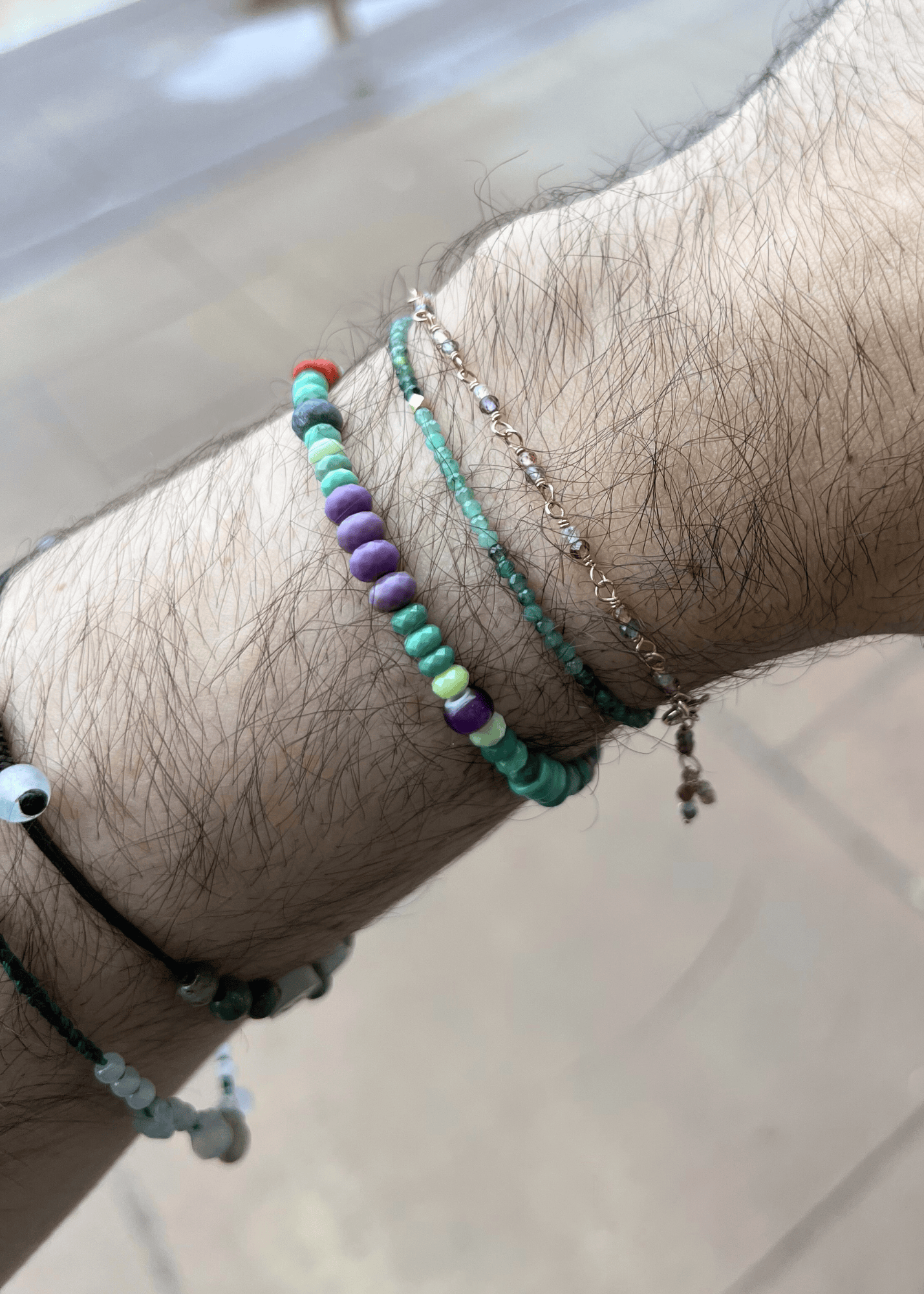 Close-up of a wrist wearing multiple beaded bracelets on a neutral background